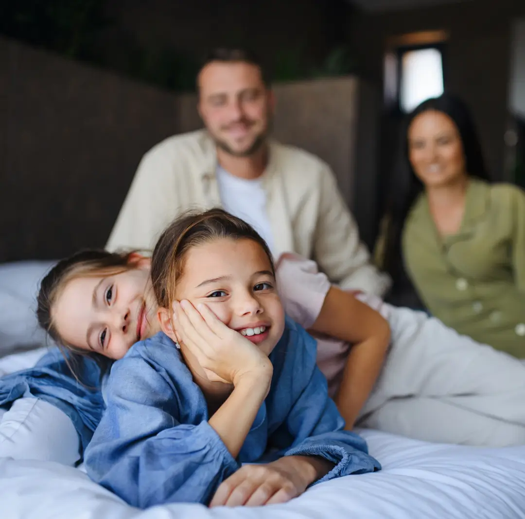 Happy family with two children relaxing on bed, showing confidence and comfort after using a gentle bed wetting solution to end bedwetting.