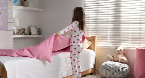 Child helping to put fresh sheets on their bed in the morning